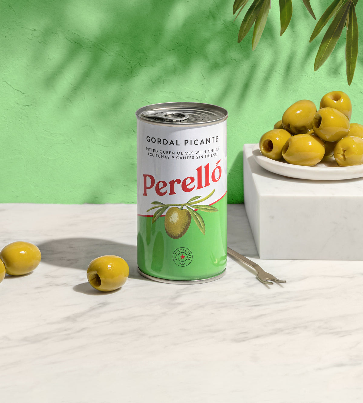 Can of Perello Gordal Picante olives on a white surface with green background, available at Blenheim Vintners.