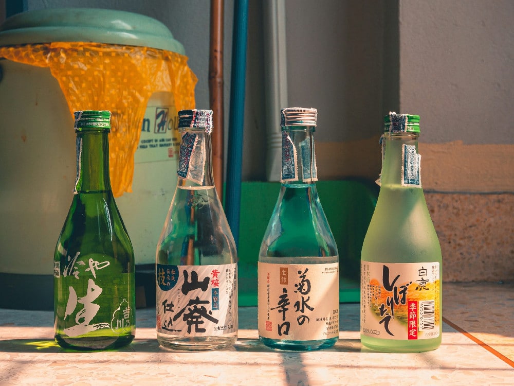 Four green bottles of Japanese Sake with labels on a concrete surface